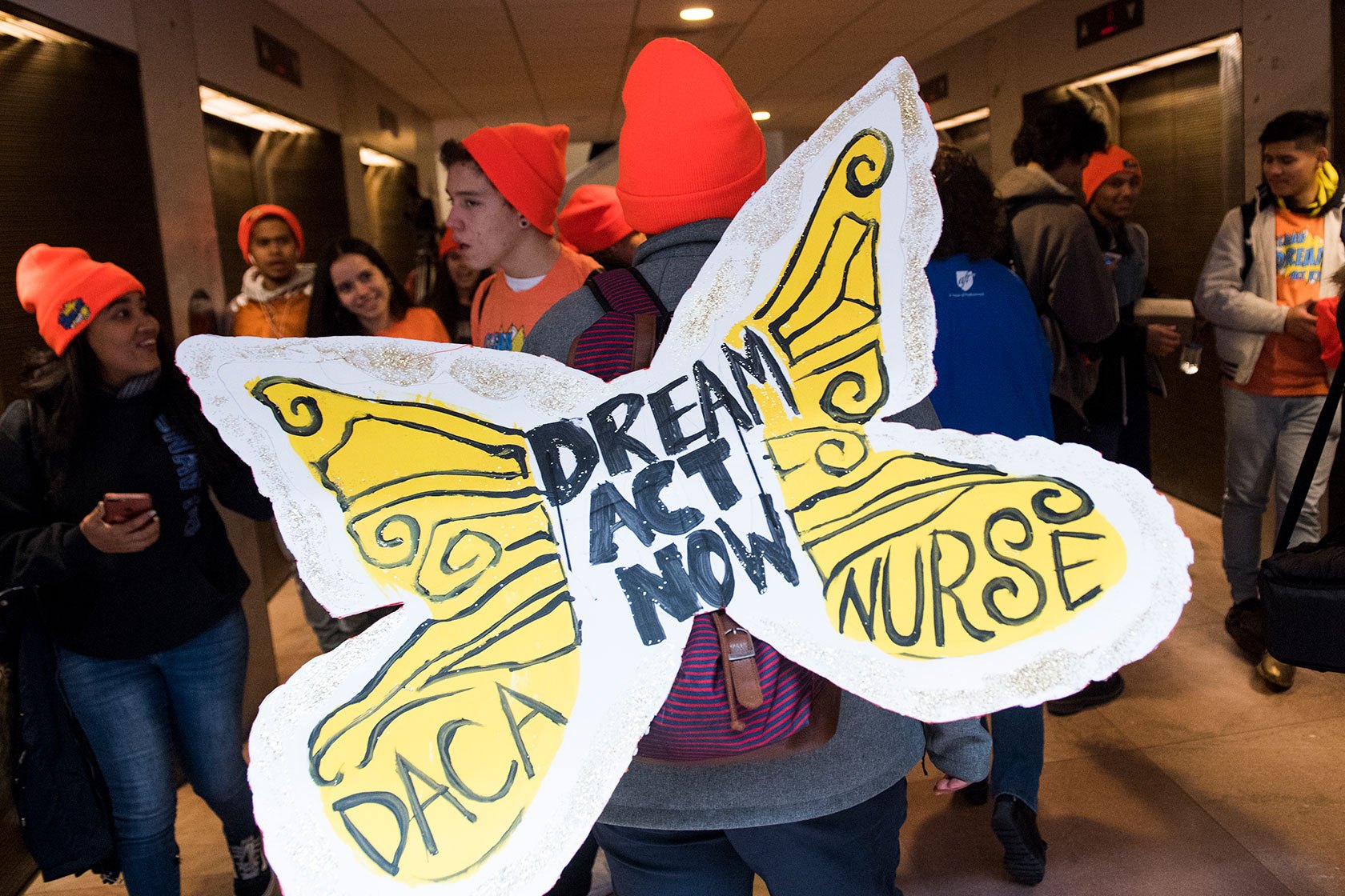 Demonstrators, one with back to camera wearing yellow butterfly wings that read 